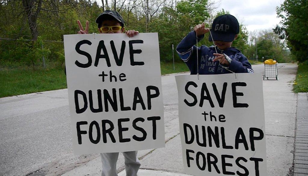 Children holding signs that say 'Save the Dunlap Forest'