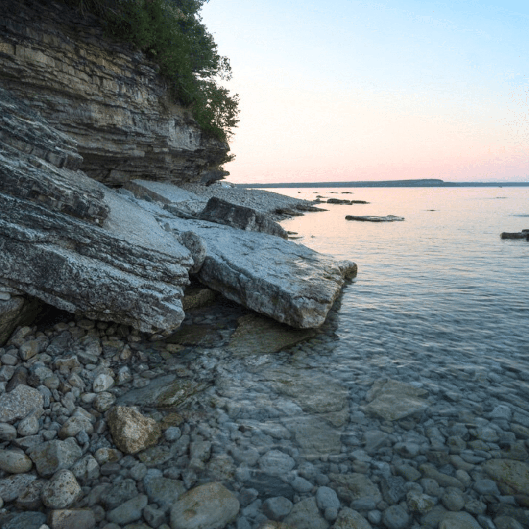 A rocky shore with trees in the sunset