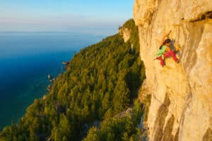 A person rock climbing a cliff next to the forest