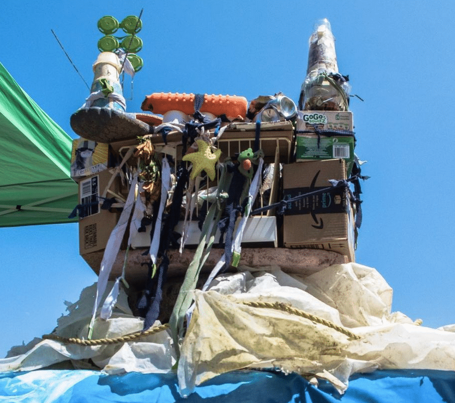 A sculpture made of plastic waste sits in front of a blue sky