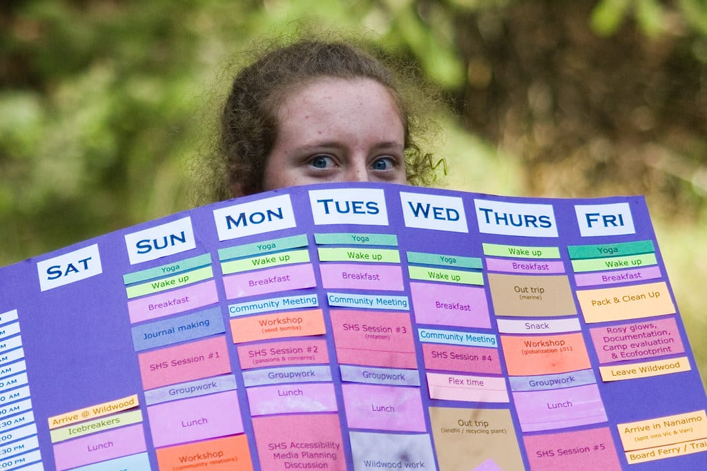 Girl's head peaking over a colorful, weekly schedule